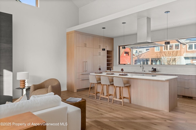 kitchen featuring a kitchen island, pendant lighting, island exhaust hood, light brown cabinets, and light hardwood / wood-style flooring