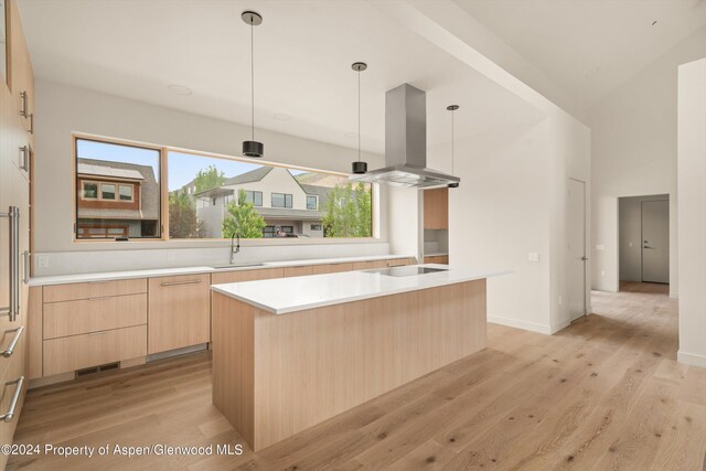 kitchen featuring island range hood, a kitchen island, sink, and hanging light fixtures