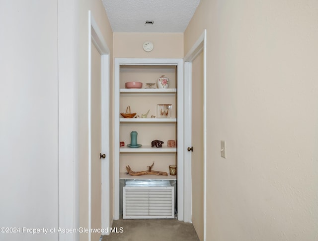 hallway featuring carpet, built in shelves, and a textured ceiling