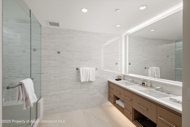 bathroom with a shower with door, vanity, and tile walls