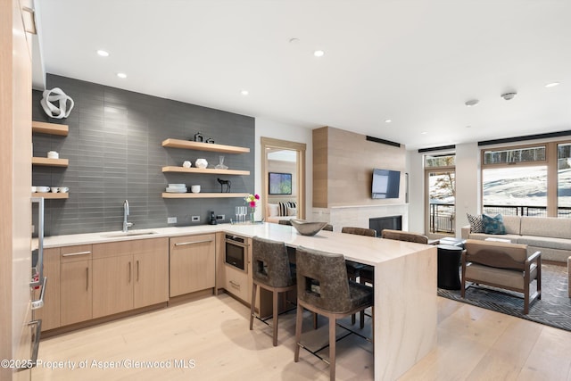 kitchen with light brown cabinets, a kitchen bar, kitchen peninsula, and light hardwood / wood-style flooring