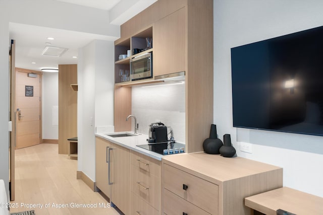 kitchen featuring light brown cabinets, stainless steel microwave, black electric stovetop, sink, and light hardwood / wood-style flooring