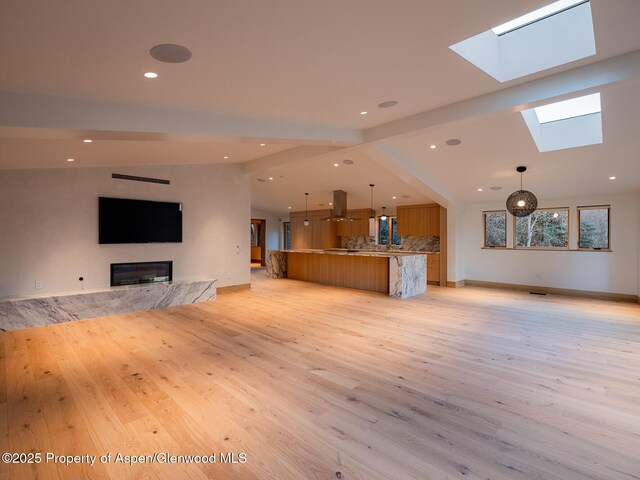 unfurnished living room featuring light wood-style floors, recessed lighting, a glass covered fireplace, and a skylight