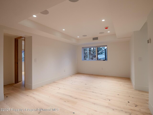 empty room with recessed lighting, a raised ceiling, light wood finished floors, and visible vents