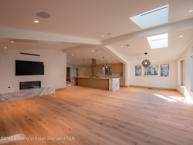 unfurnished living room featuring recessed lighting, a skylight, baseboards, and light wood-style floors
