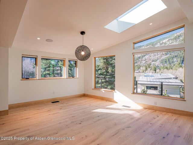 interior space featuring vaulted ceiling with skylight, visible vents, wood finished floors, baseboards, and recessed lighting