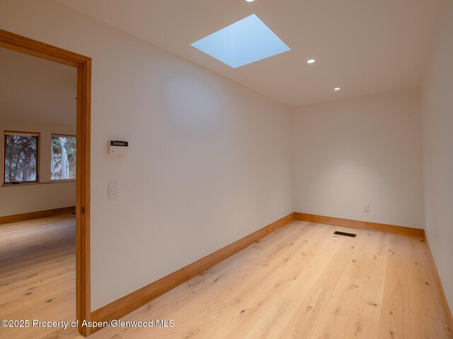 empty room featuring visible vents, a skylight, light wood-type flooring, baseboards, and recessed lighting