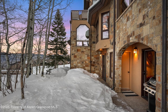 view of snowy exterior featuring stone siding and a balcony