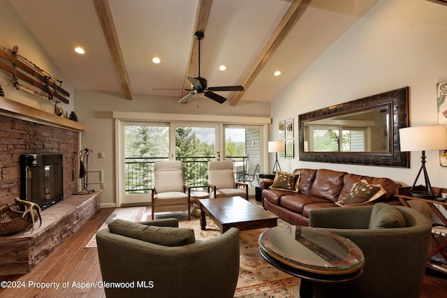 living room with a stone fireplace, ceiling fan, wood-type flooring, and vaulted ceiling with beams