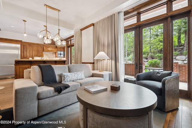 living room with hardwood / wood-style floors, a notable chandelier, lofted ceiling, and french doors