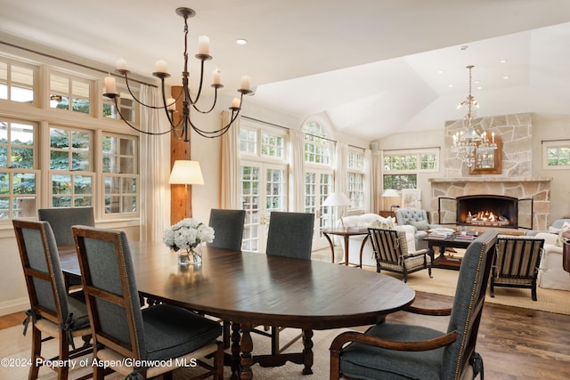 dining room with hardwood / wood-style floors, a stone fireplace, lofted ceiling, and a notable chandelier