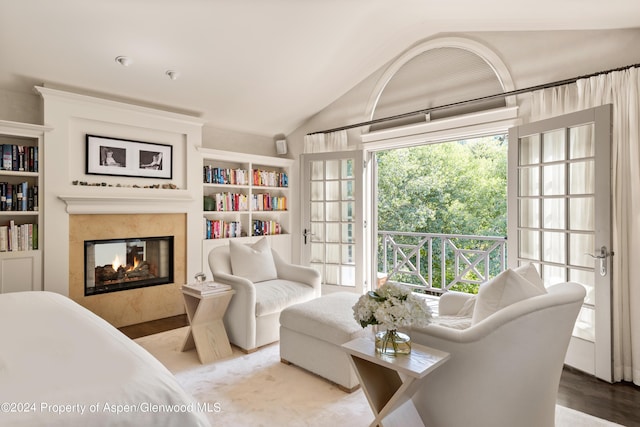 sitting room with a high end fireplace, built in shelves, light wood-type flooring, and vaulted ceiling