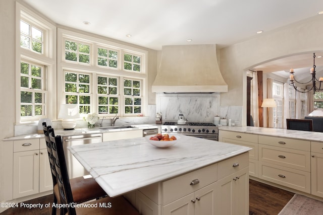 kitchen featuring decorative backsplash, premium range hood, light stone counters, stainless steel appliances, and sink