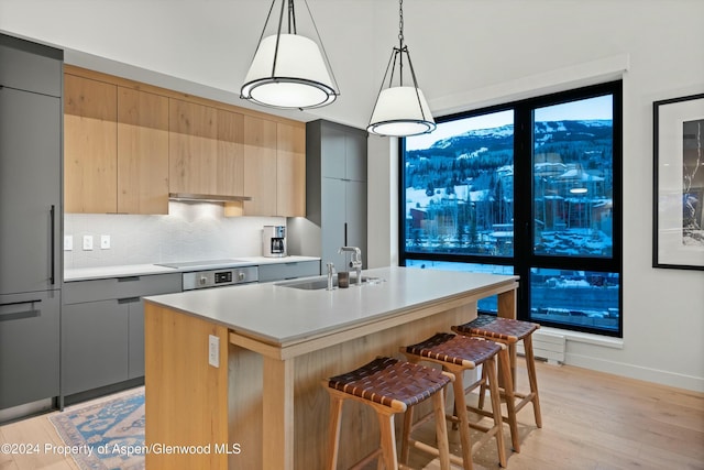 kitchen with gray cabinetry, a center island with sink, built in fridge, sink, and decorative light fixtures