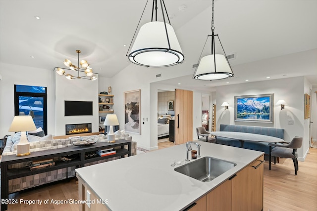 kitchen with sink, hanging light fixtures, light hardwood / wood-style flooring, vaulted ceiling, and an island with sink