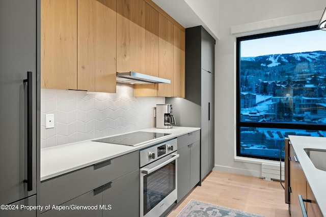 kitchen featuring decorative backsplash, appliances with stainless steel finishes, exhaust hood, light hardwood / wood-style flooring, and gray cabinets