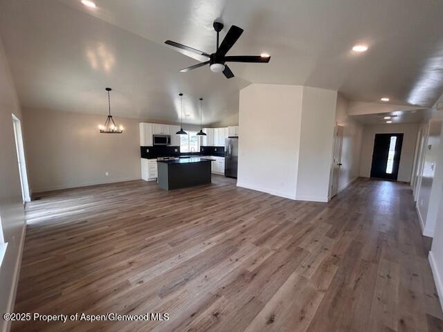 326 W 30th St, Rifle, CO 81650 - unfurnished living room featuring lofted ceiling, baseboards, wood finished floors, a ceiling fan, and a chandelier