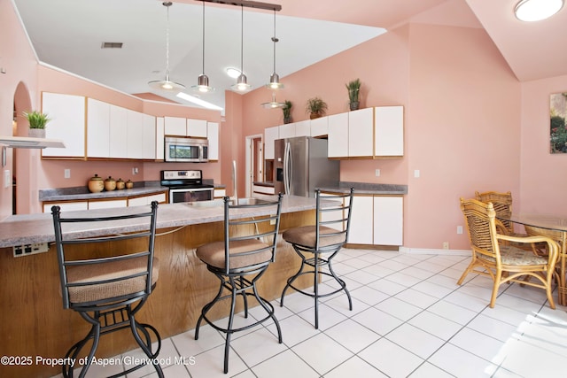kitchen with appliances with stainless steel finishes, lofted ceiling, white cabinetry, a kitchen breakfast bar, and pendant lighting