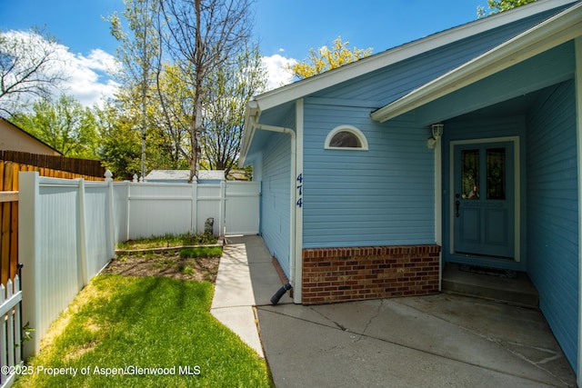 doorway to property featuring fence, brick siding, and a patio area