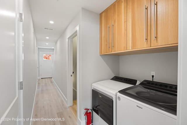 laundry area with cabinets, light wood-type flooring, and washing machine and clothes dryer