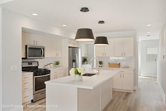 kitchen featuring pendant lighting, sink, light wood-type flooring, an island with sink, and stainless steel appliances