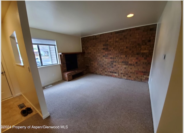 unfurnished living room with light carpet, a fireplace, and brick wall