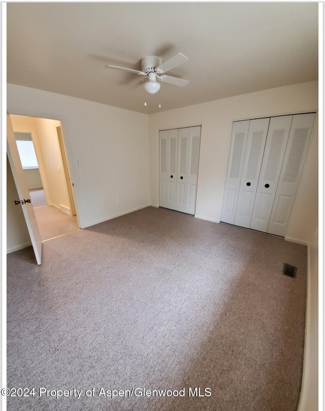 unfurnished bedroom featuring multiple closets, ceiling fan, and carpet floors