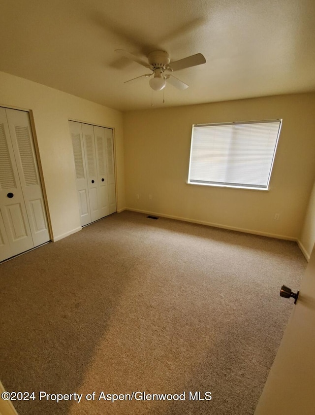 unfurnished bedroom with carpet floors, two closets, and ceiling fan