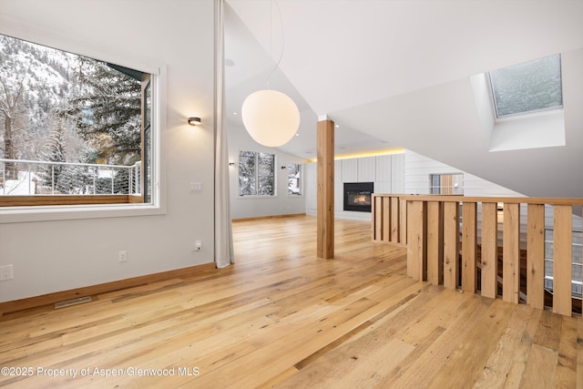 bonus room with vaulted ceiling with skylight and light wood-type flooring