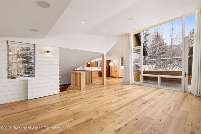 unfurnished living room featuring light wood-type flooring, wooden walls, and lofted ceiling