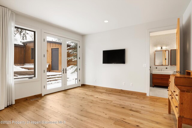 interior space with light hardwood / wood-style floors, access to exterior, connected bathroom, and french doors