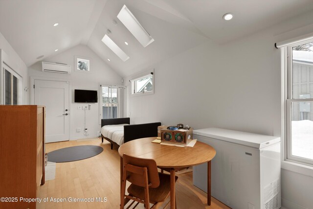 dining area featuring lofted ceiling with skylight, a wall unit AC, and light hardwood / wood-style flooring