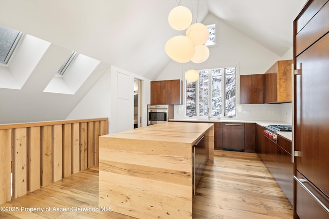 kitchen with a center island, light wood-type flooring, decorative light fixtures, and appliances with stainless steel finishes