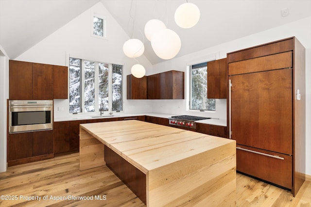 kitchen with appliances with stainless steel finishes, sink, pendant lighting, a center island, and light hardwood / wood-style floors