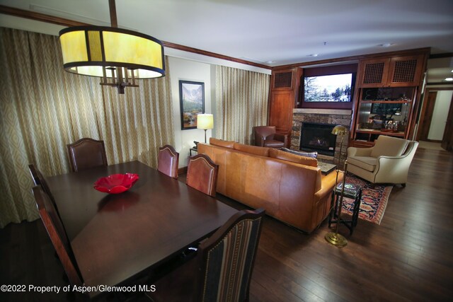 dining room with dark hardwood / wood-style floors, a stone fireplace, and ornamental molding