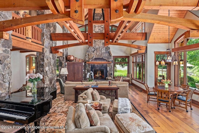 living room featuring a fireplace, hardwood / wood-style flooring, high vaulted ceiling, a notable chandelier, and beamed ceiling