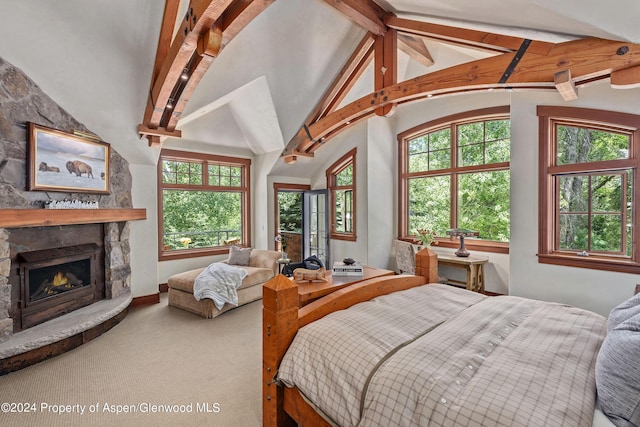 carpeted bedroom with lofted ceiling with beams, a stone fireplace, and multiple windows