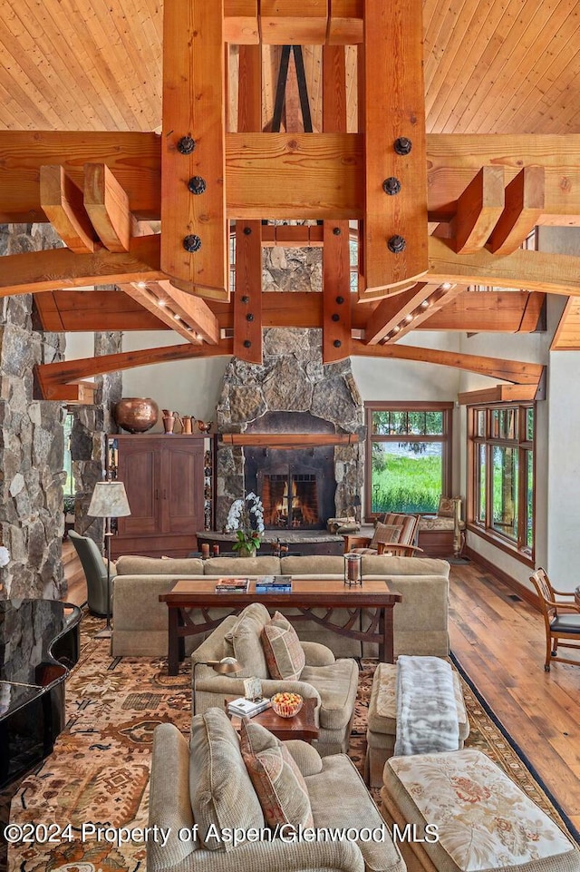 living room featuring a stone fireplace, hardwood / wood-style floors, beamed ceiling, and high vaulted ceiling