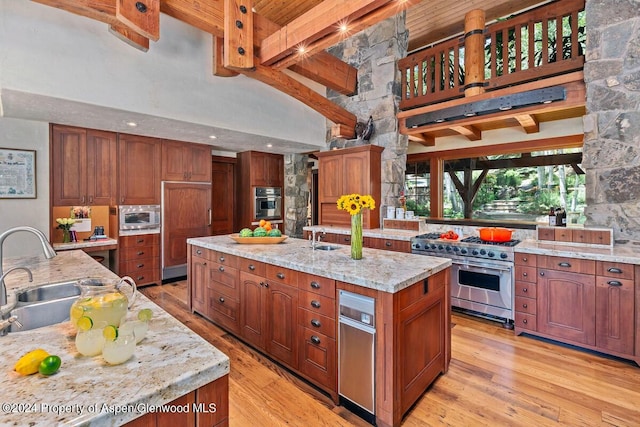 kitchen featuring a kitchen island with sink, high vaulted ceiling, sink, appliances with stainless steel finishes, and light stone counters