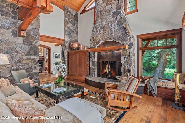 living room featuring beam ceiling, hardwood / wood-style flooring, high vaulted ceiling, wooden ceiling, and a stone fireplace