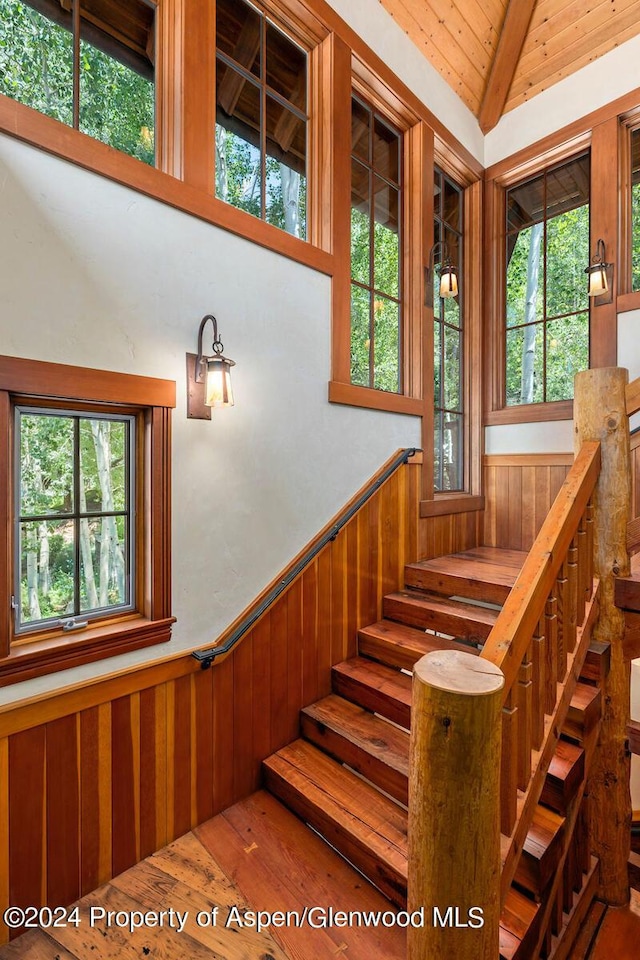 staircase featuring vaulted ceiling with beams, wood walls, wooden ceiling, and wood-type flooring