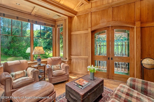 sitting room with beam ceiling, light wood-type flooring, wooden walls, and coffered ceiling