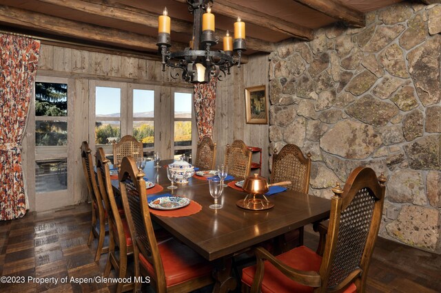 dining space featuring beamed ceiling, dark parquet flooring, a notable chandelier, and wood walls