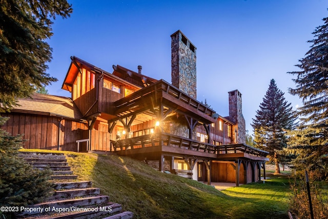 back house at dusk featuring a wooden deck and a lawn