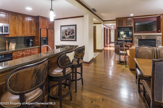 kitchen with a stone fireplace, dark hardwood / wood-style floors, decorative light fixtures, decorative backsplash, and black appliances