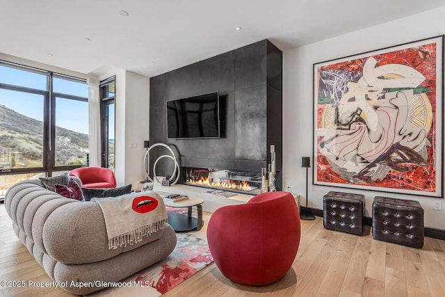 living room with a large fireplace, floor to ceiling windows, and light hardwood / wood-style floors