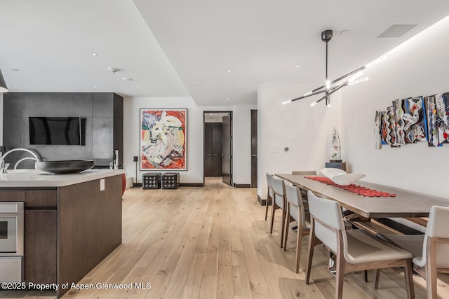 kitchen featuring sink, light wood-type flooring, dark brown cabinetry, wall oven, and an inviting chandelier