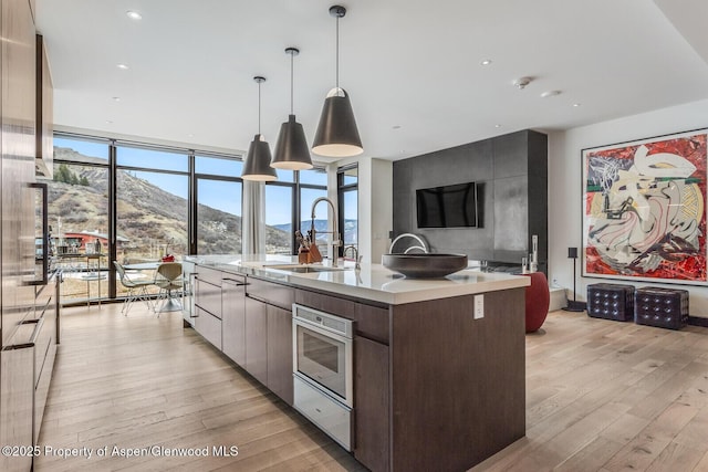 kitchen with pendant lighting, sink, a kitchen island with sink, wall oven, and light hardwood / wood-style flooring