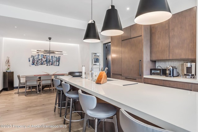 kitchen featuring tasteful backsplash, hanging light fixtures, light hardwood / wood-style flooring, and a kitchen breakfast bar