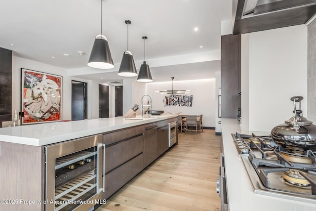 kitchen with pendant lighting, an island with sink, sink, wine cooler, and light hardwood / wood-style flooring